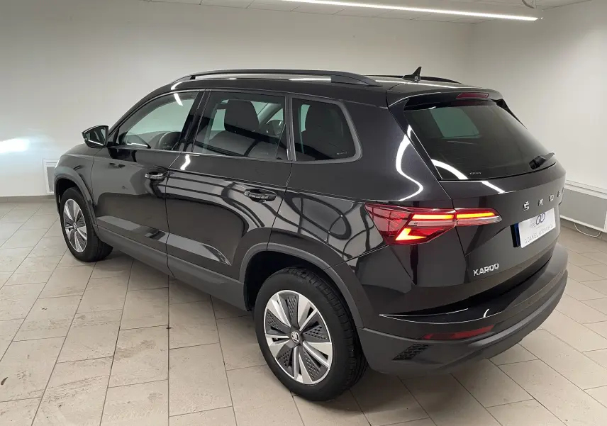 Vue 3/4 arrière droite d'un Skoda Karoq noir nacré avec feux arrière allumés dans un intérieur neutre.