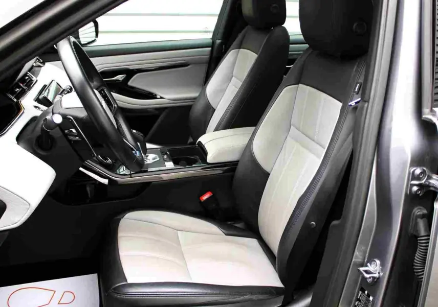 Vue intérieure côté conducteur du Range Rover Evoque 2023 gris métal, sièges bi-ton cuir noir et beige, tableau de bord moderne.