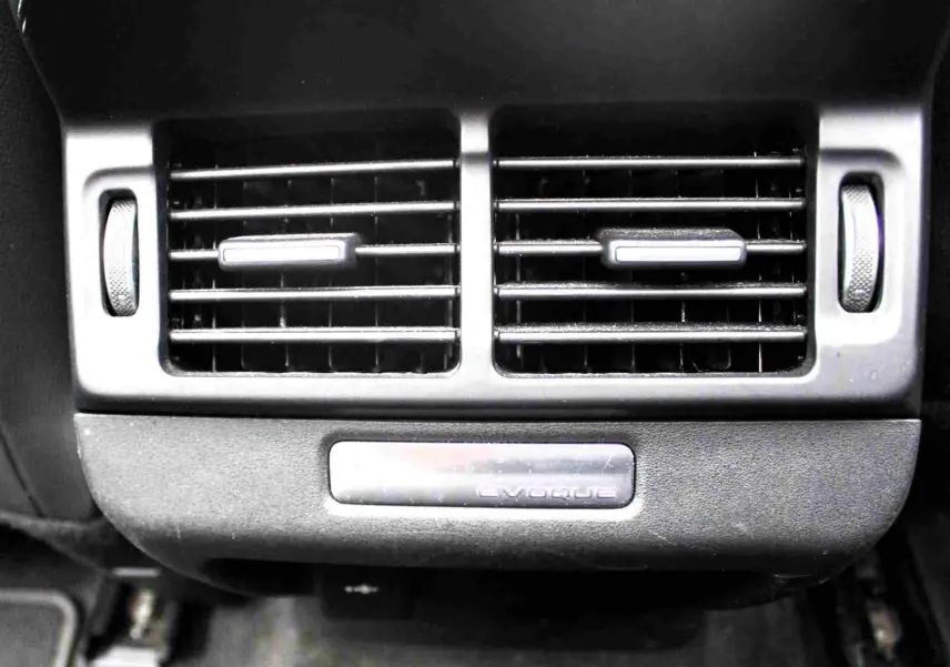 Gros plan sur la grille d’aération arrière avec plaque Range Rover Evoque, intérieur noir du SUV hybride gris métal 2023.