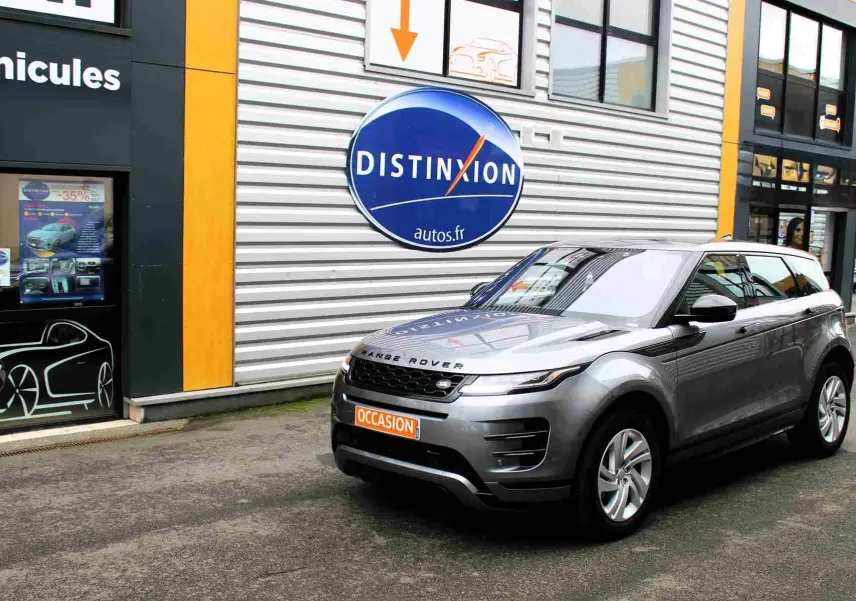 Range Rover Evoque gris métal 2023 en 3/4 avant droit, hybride rechargeable, devant un bâtiment commercial.