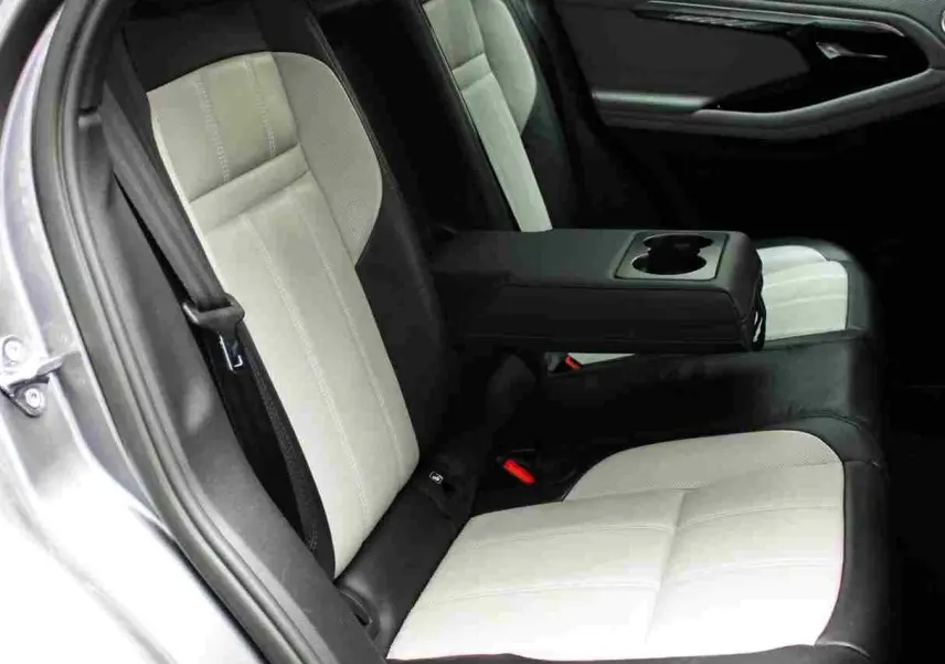 Vue intérieure côté gauche des sièges arrière bicolores noirs et gris du Range Rover Evoque 2023 gris métal avec accoudoir central rabattable.