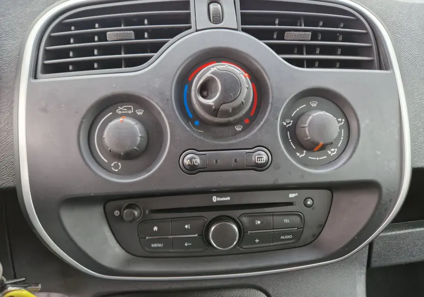 Gros plan sur la console centrale du Renault Kangoo blanc 2019, montrant les commandes de climatisation et radio Bluetooth.