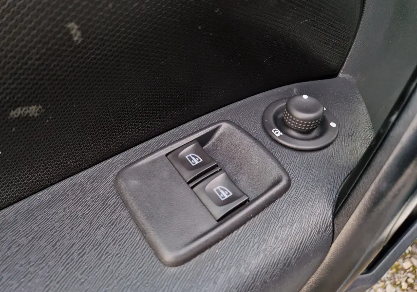 Gros plan sur les commandes électriques des vitres et le réglage des rétroviseurs côté conducteur d’un Renault Kangoo blanc.