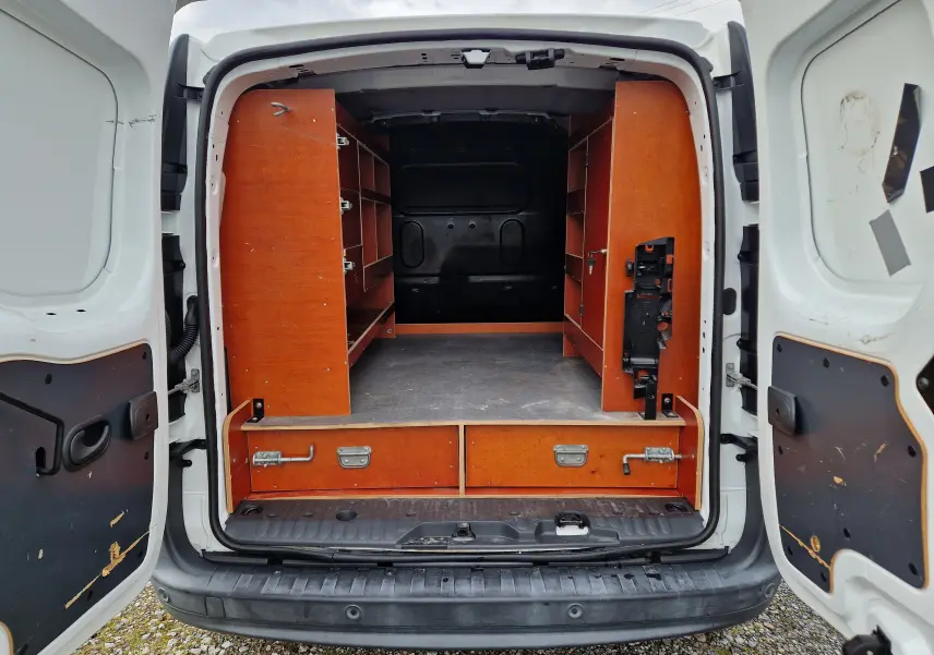 Vue arrière ouverte du Renault Kangoo blanc 2019, montrant l'aménagement intérieur avec étagères en bois et rangements.