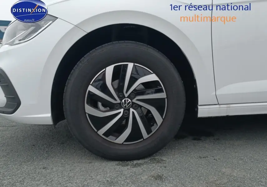 Gros plan sur la roue avant gauche et la jante alliage noire et argentée d'une Volkswagen Polo blanche.