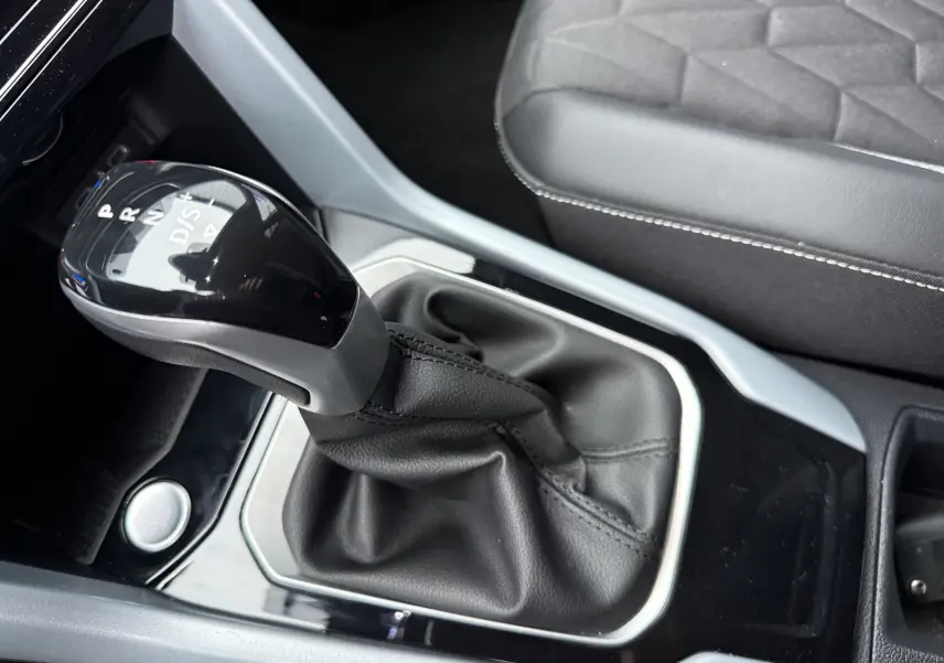Gros plan sur le levier de vitesses automatique noir et gris du Volkswagen T-Roc 2025, avec sellerie noire visible.