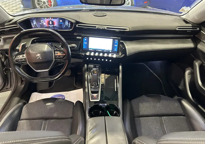 Vue intérieure avant du Peugeot 508 SW avec tableau de bord numérique, volant compact et finition carbone noire.