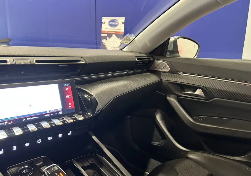 Vue intérieure côté passager du tableau de bord et de la porte d’une Peugeot 508 SW avec finition carbone et écran tactile allumé.