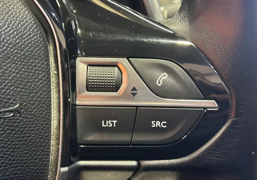 Gros plan sur les commandes au volant côté gauche de la Peugeot 508 SW, finition noire brillante et cuir.