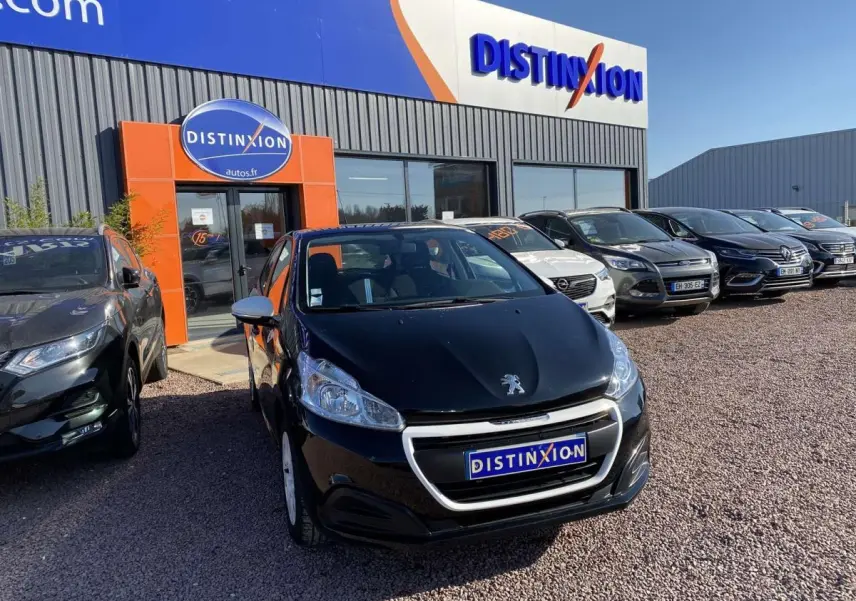 Peugeot 208 noire vue de face, avec jonc de calandre blanc, stationnée devant un concessionnaire Distinxion.