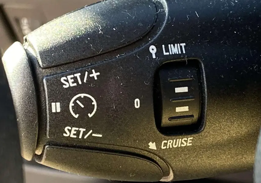 Gros plan sur la commande du régulateur et limiteur de vitesse de la Peugeot 208 noire de 2015.