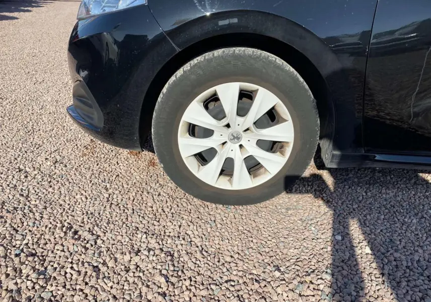 Gros plan sur la roue avant droite d'une Peugeot 208 noire, avec jante en acier et enjoliveur blanc.