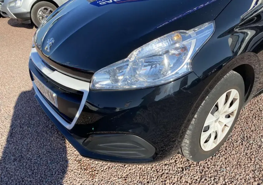 Vue 3/4 avant droit d'une Peugeot 208 noire avec jonc de calandre blanc et phare allumé.