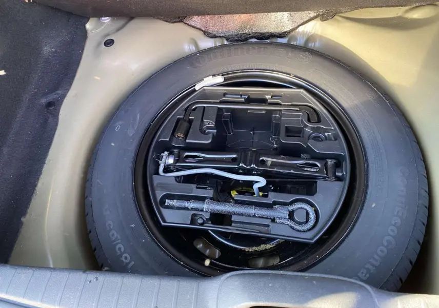 Gros plan sur la roue de secours acier 15 pouces noire avec kit d'outils dans le coffre d'une Peugeot 208 noire.