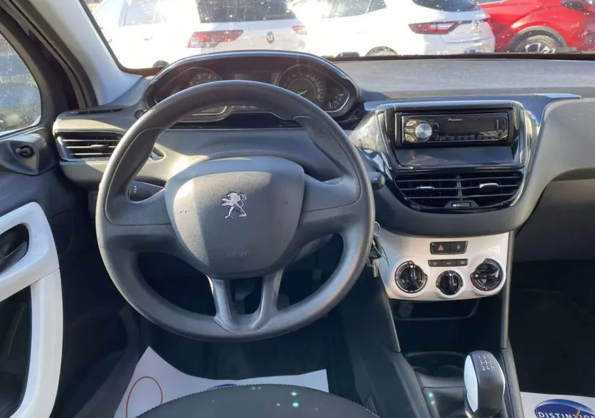 Vue intérieure centrée sur le volant Peugeot 208 noir, tableau de bord avec autoradio Pioneer et commande manuelle de vitesses.