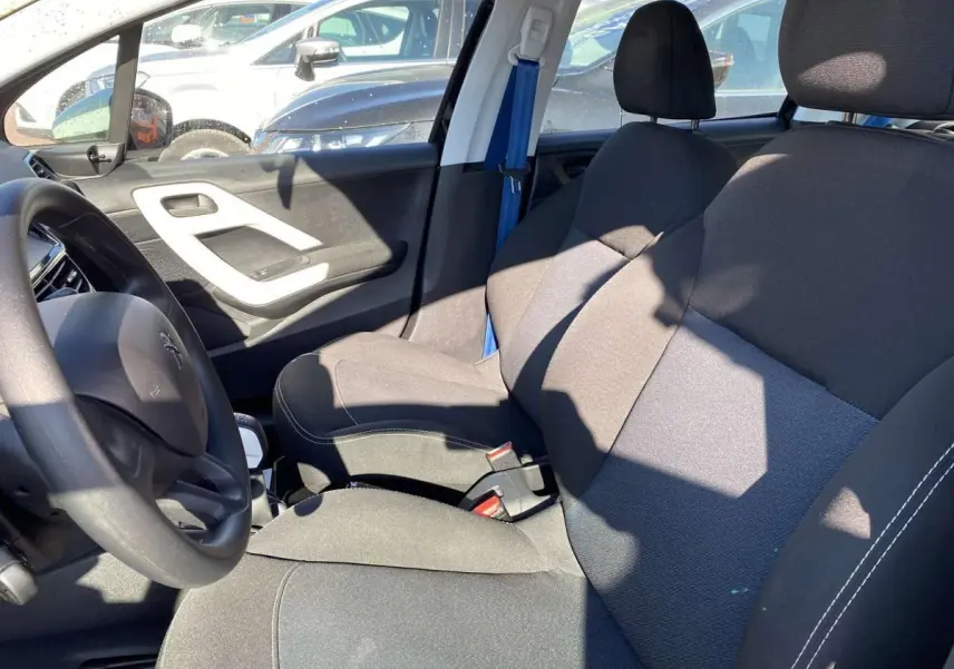 Vue intérieure côté conducteur de la Peugeot 208 noire, montrant les sièges avant et le volant au soleil.