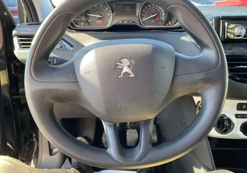 Vue rapprochée du volant noir de la Peugeot 208 2015 avec tableau de bord et commandes de climatisation visibles.
