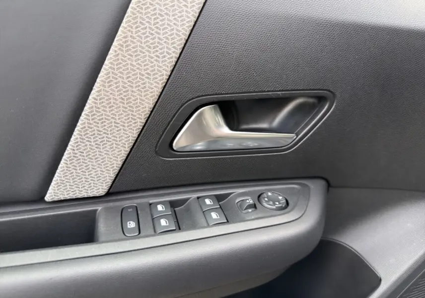 Gros plan sur la poignée intérieure et les commandes de fenêtre côté conducteur d'une Citroën C4 noire 2023.