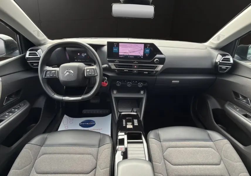 Vue intérieure avant de la Citroën C4 noire 2023, tableau de bord moderne avec écran tactile central et volant cuir multifonctions.