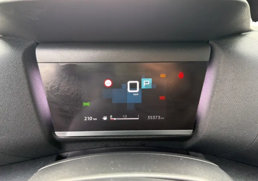 Affichage numérique du tableau de bord central de la Citroën C4 noir, montrant la vitesse à 0 km/h et l'autonomie restante.