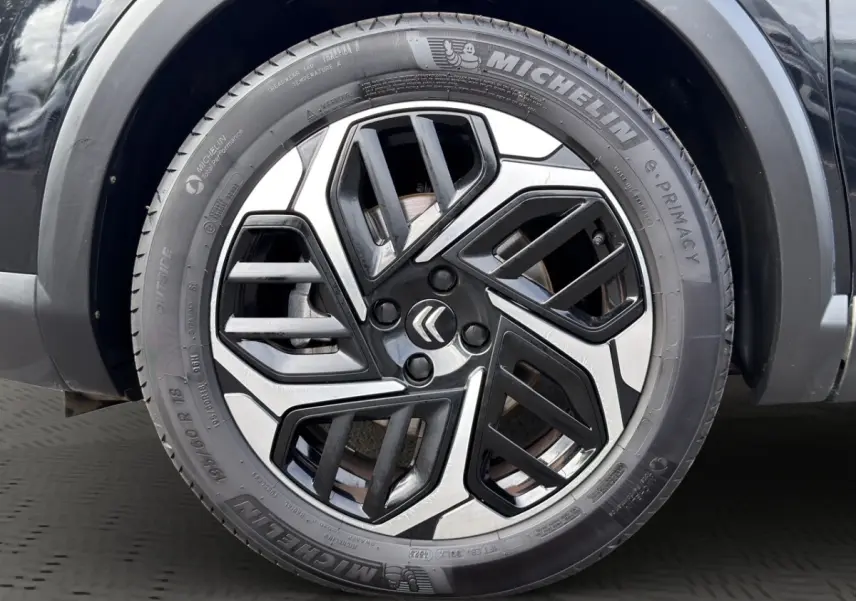 Gros plan sur la roue avant droite noire d'une Citroën C4 2023 avec jante alliage bicolore et pneu Michelin.