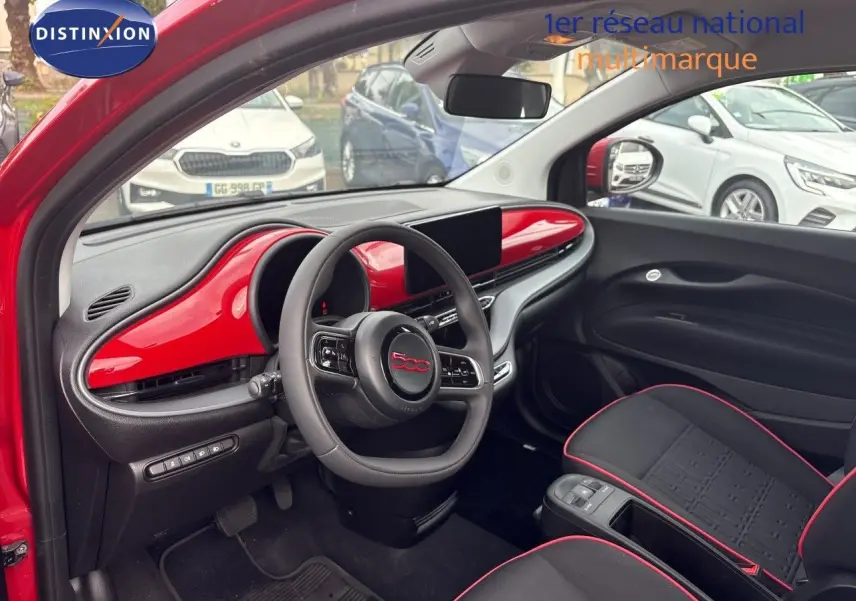 Vue intérieure côté conducteur de la FIAT 500e rouge 2024, tableau de bord et volant avec insert rouge brillant.
