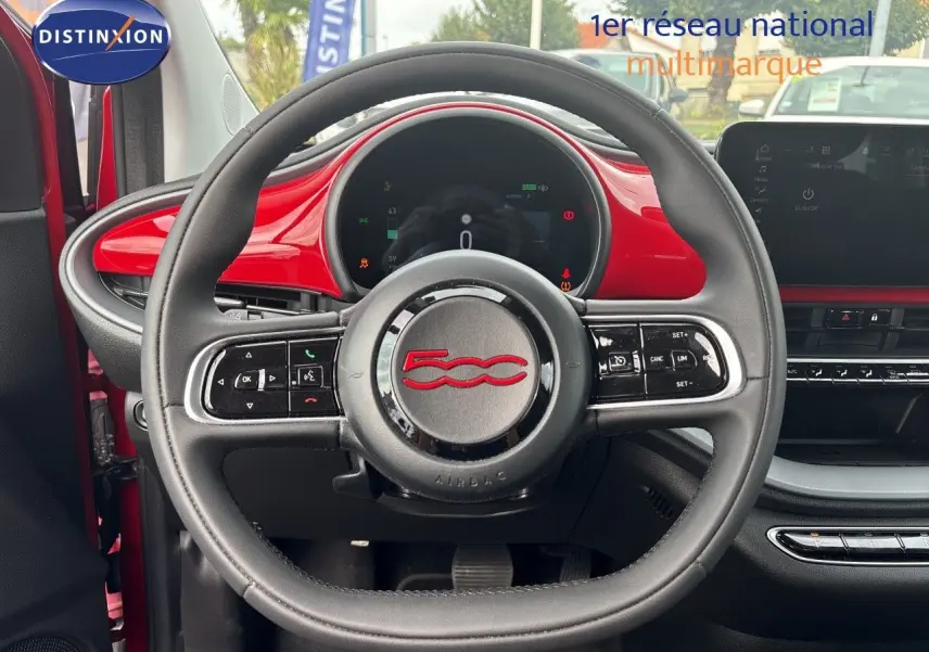 Vue intérieure centrée sur le volant noir avec logo rouge 500, tableau de bord et garniture rouge vif FIAT 500e 2024.