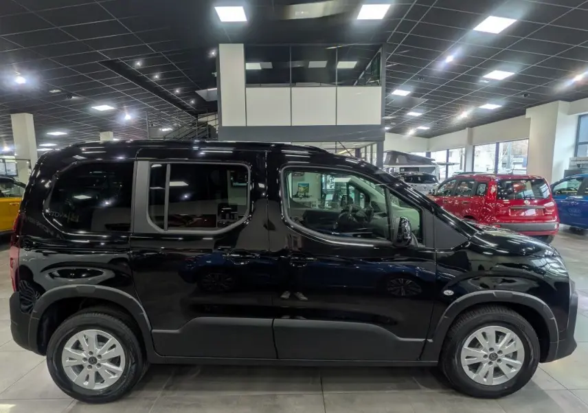 Profil droit d’un Peugeot Rifter Allure noir Perla Nera 2026 en showroom, avec jantes argentées et vitres teintées.
