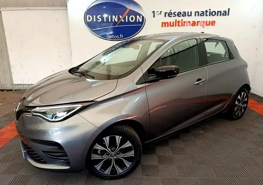 Renault ZOE gris clair en 3/4 avant droit, avec jantes alliage et phares LED, en intérieur showroom.