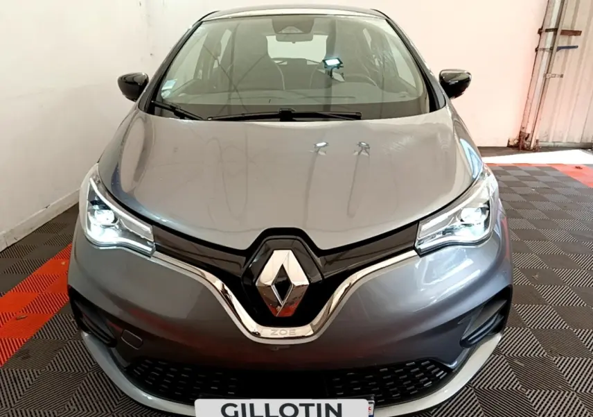 Vue frontale d'une Renault ZOE gris clair avec phares LED allumés dans un garage fermé.