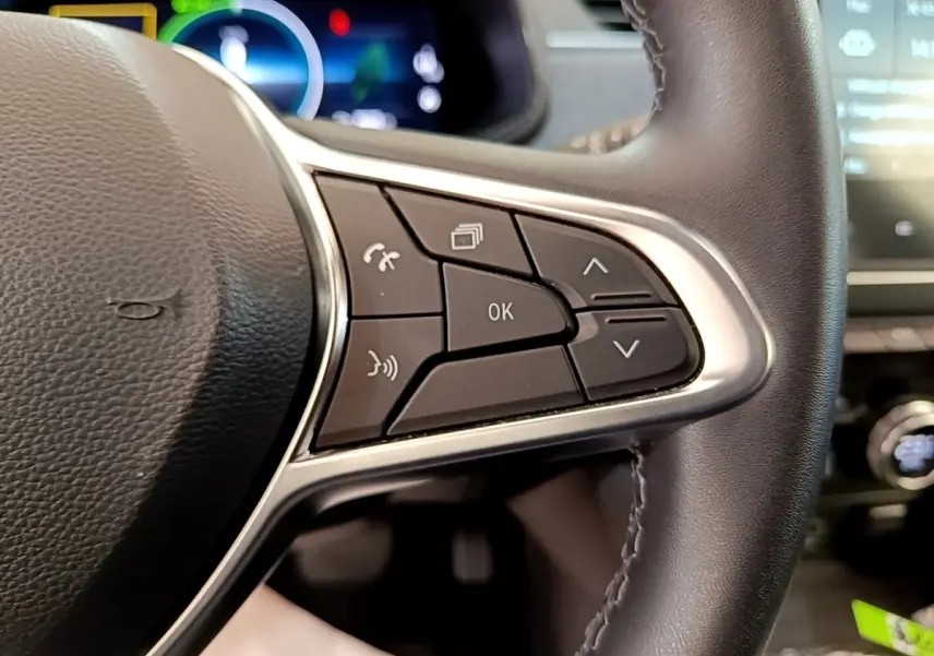 Gros plan sur les commandes au volant à droite de la Renault ZOE gris clair, avec affichage numérique en arrière-plan.