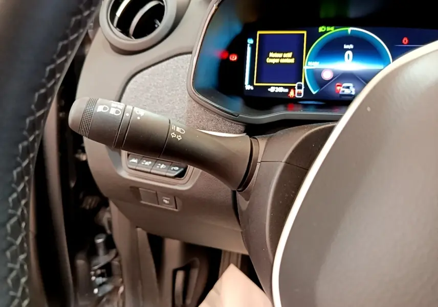 Gros plan sur la manette de clignotant à gauche du volant, avec le combiné d'instruments numérique éclairé de la Renault ZOE gris clair.