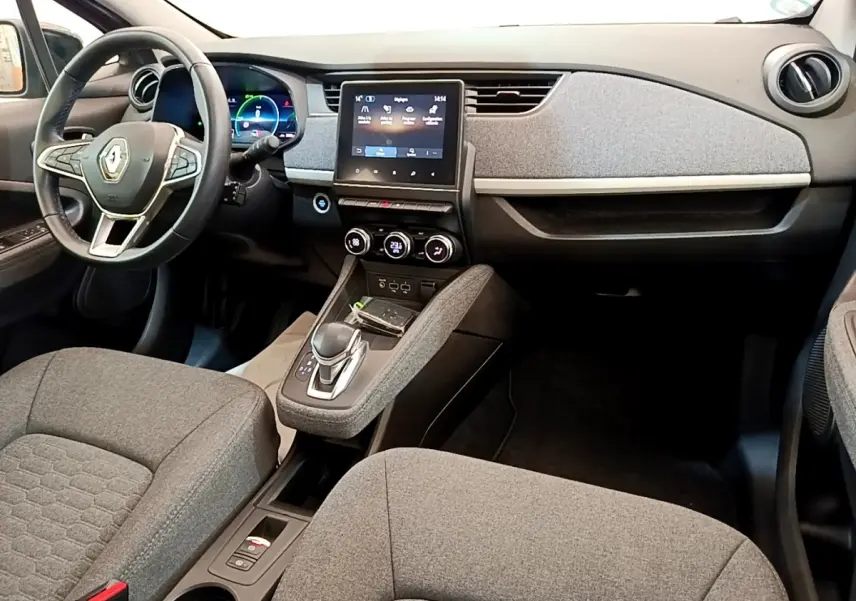 Vue intérieure avant de la Renault ZOE gris clair, montrant le tableau de bord avec écran tactile central et volant multifonctions.