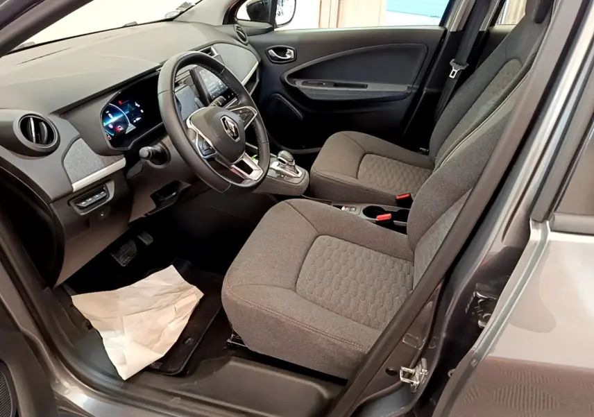 Vue intérieure côté conducteur de la Renault ZOE gris clair, montrant les sièges tissu et le tableau de bord avec écran tactile.