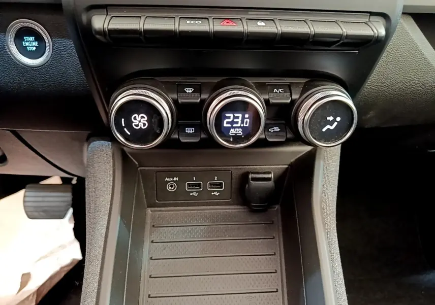 Vue rapprochée du tableau de bord central de la Renault ZOE gris clair, avec commandes climatisation et bouton démarrage visibles.