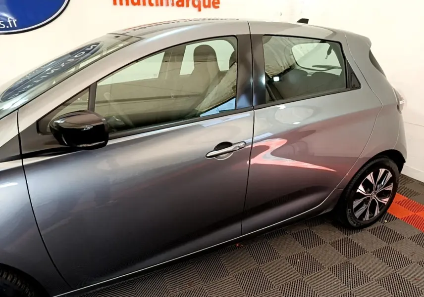 Profil côté gauche d'une Renault ZOE gris clair 2022, avec rétroviseur noir et jantes alliage visibles.