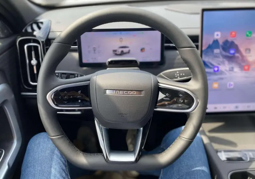 Vue intérieure centrée sur le volant noir du JAECOO J7 2026 avec écrans digitaux en arrière-plan.