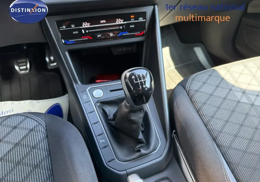 Vue intérieure centrée sur la console centrale d'une Volkswagen Polo rouge Roi 2023 avec levier de vitesse manuel et climatisation digitale.