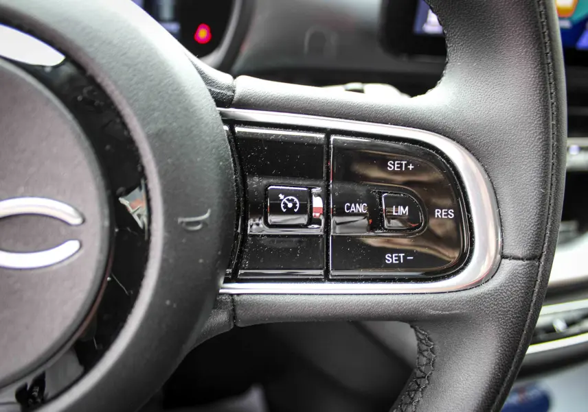 Gros plan sur les commandes de régulateur de vitesse au volant cuir noir de la Fiat 500 électrique gris minéral 2023.
