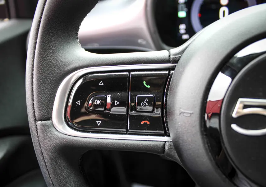 Gros plan sur les commandes gauche du volant noir de la Fiat 500 électrique gris minéral 2023, avec boutons multifonctions.