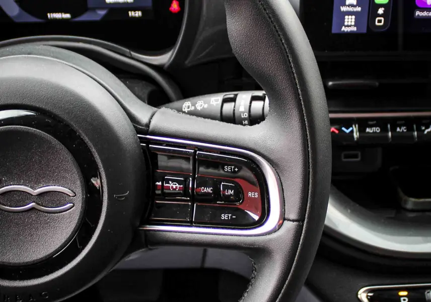 Vue rapprochée du volant et tableau de bord numérique de la Fiat 500 électrique 2023, intérieur noir avec écran tactile CarPlay.