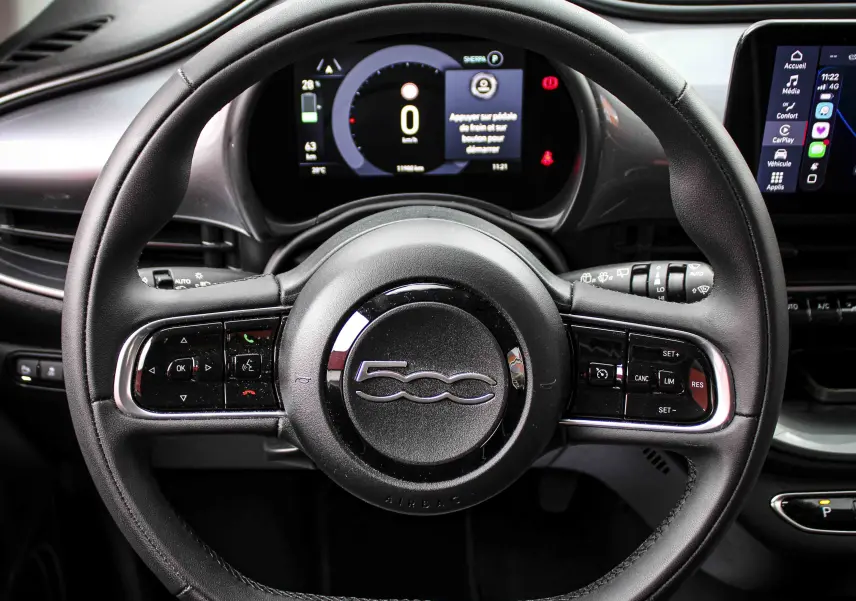 Vue rapprochée du volant noir de la Fiat 500 électrique 2023 avec tableau de bord digital et écran tactile central.