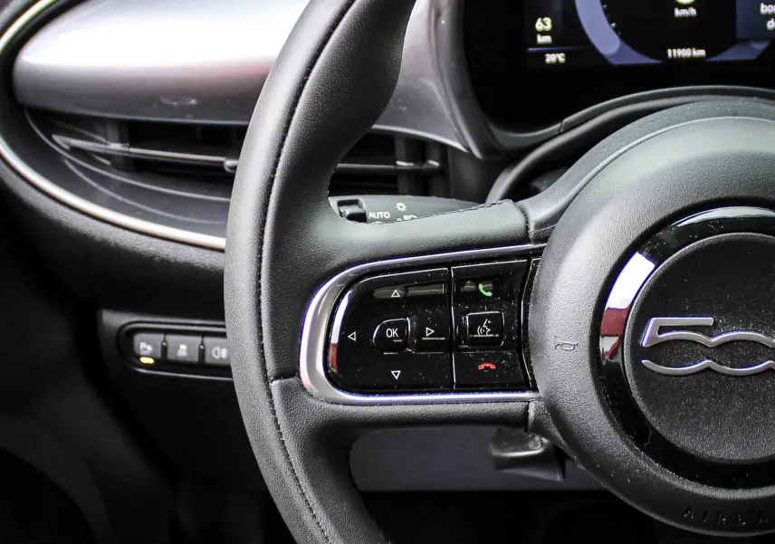 Gros plan sur le volant noir et le tableau de bord numérique de la FIAT 500 électrique 2023, ambiance intérieure moderne.