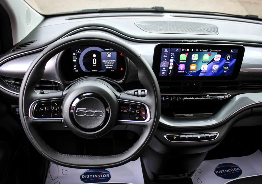 Vue intérieure du tableau de bord de la Fiat 500 électrique 2023, avec volant noir et écran tactile central lumineux.