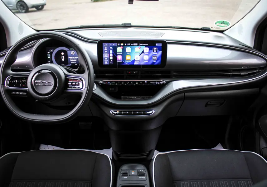 Vue frontale de l’habitacle de la FIAT 500 électrique gris minéral, avec tableau de bord numérique et écran tactile central.