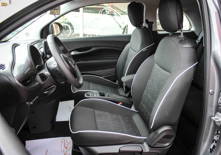 Vue intérieure côté conducteur de la FIAT 500 électrique gris minéral, sièges tissu noir avec surpiqûres blanches.