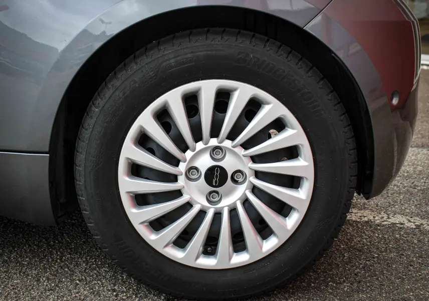 Gros plan sur la roue avant gauche d’une FIAT 500 électrique gris minéral métal, avec jante argentée à rayons fins.