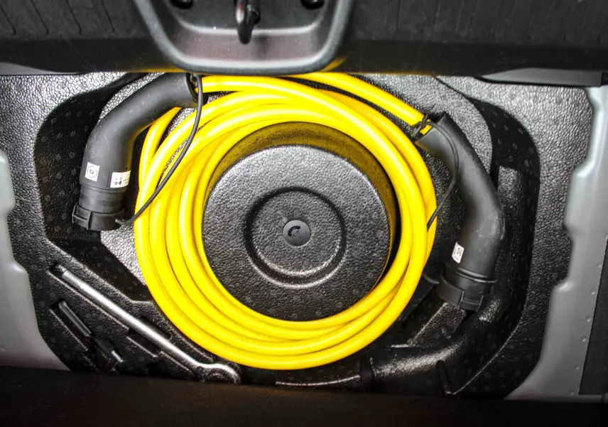 Gros plan sur le câble de recharge jaune enroulé dans le coffre d'une Fiat 500 électrique gris minéral 2023.