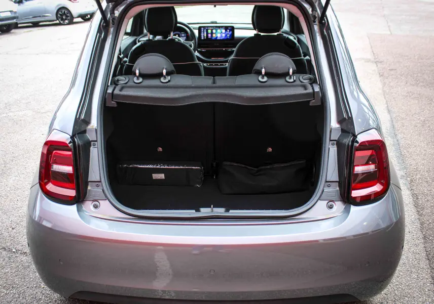 Vue arrière ouverte sur le coffre d'une FIAT 500 électrique gris minéral métal, avec intérieur noir et sièges visibles.