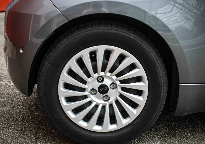 Gros plan sur la roue arrière gauche d'une FIAT 500 électrique gris minéral métal avec jante argentée à rayons fins.